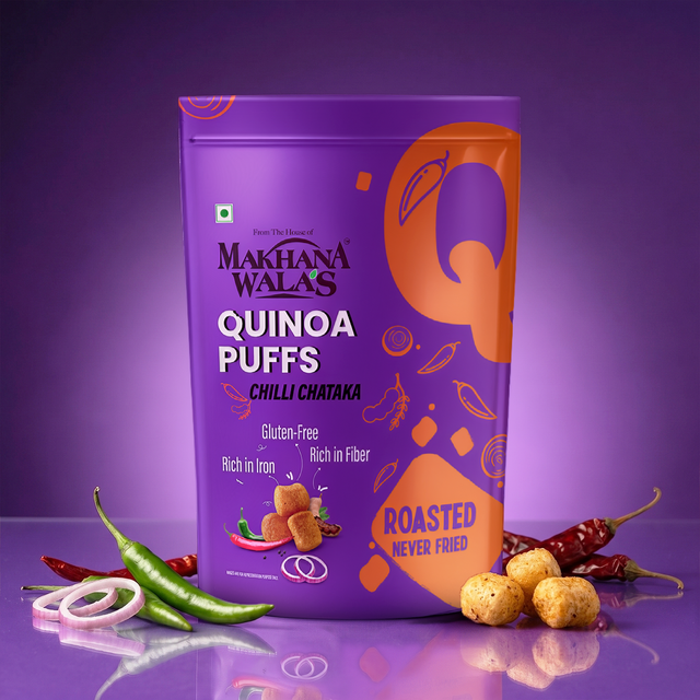 A purple bag of Makhana Walas Quinoa Puffs (Chilli Chataka) is shown on a reflective purple surface with green chilies, red chilies, onion rings, and roasted puffs as props.