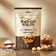 A stand-up pouch of Makhana Wala's Roasted Salt-n-Pepper foxnut and corgon nut snack, styled on a reflective surface with bowls of whole and ground spices and salt in the foreground against a warm beige background.