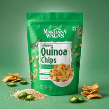A green stand-up pouch of Makhana Walas Jalapeno Quinoa Chips is centered on a green background, surrounded by loose chips, sliced jalapeño peppers, and quinoa seeds. The package shows the Makhana Walas brand name and a bowl of chips on the front.