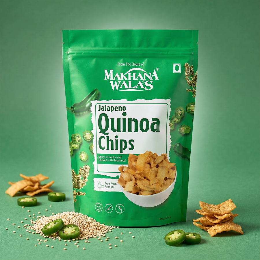 A green stand-up pouch of Makhana Walas Jalapeno Quinoa Chips is centered on a green background, surrounded by loose chips, sliced jalapeño peppers, and quinoa seeds. The package shows the Makhana Walas brand name and a bowl of chips on the front.